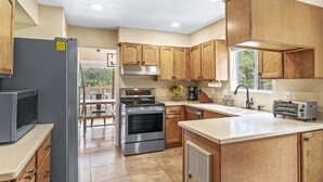 A modern kitchen with wooden cabinets, a stainless steel refrigerator, an oven, a toaster, and a window providing natural light. - Peaceful Forest Retreat· Hot Tub · Sauna · Views (Flagstaff)