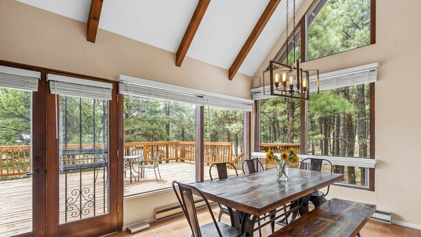 A spacious dining area with a wooden table and chairs, large windows with blinds, and a view of a deck and trees. - Peaceful Forest Retreat· Hot Tub · Sauna · Views (Flagstaff)