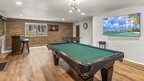 A pool table in a room with a brick wall, a dartboard, and a painting of a beach scene. - Peaceful Forest Retreat· Hot Tub · Sauna · Views (Flagstaff)