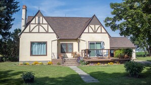 A two-story house with a prominent chimney, a front porch with a railing, and a small deck area. - The Old Farmstead (Stevensville)