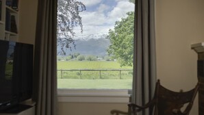A room with a window offering a view of a green field and mountains. - The Old Farmstead (Stevensville)
