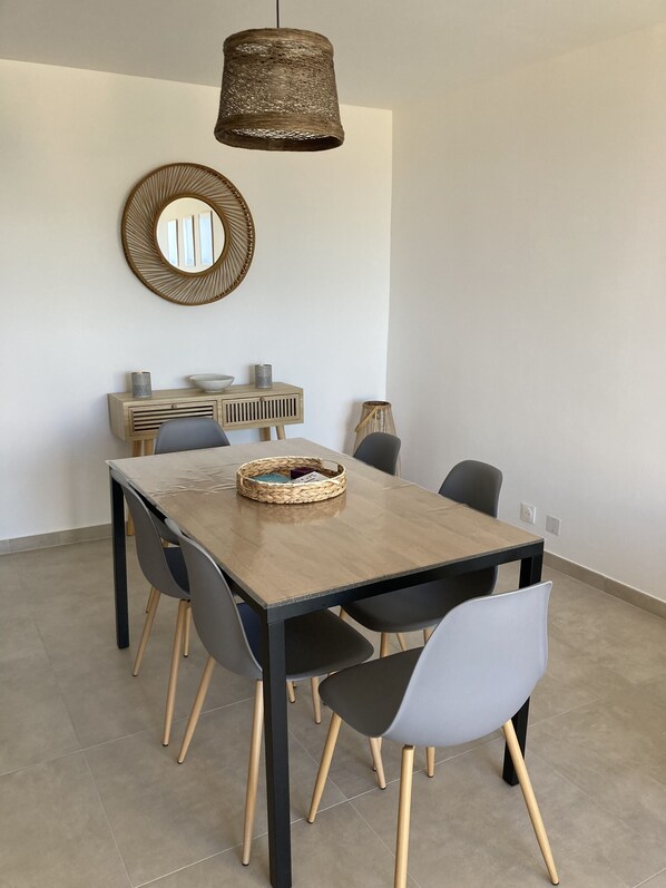 A dining area with a wooden table, six chairs, a woven basket, a round mirror, and a hanging light fixture.