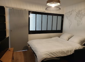 Une chambre à coucher avec un lit, une fenêtre avec des stores, une carte du monde accrochée au mur et un luminaire suspendu.