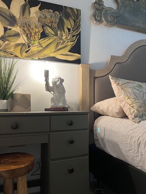 Un dormitorio con una cama, una mesita de noche con lámpara, una estatua decorativa y un cuadro colgado en la pared.