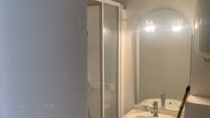 Een badkamer met een douchecabine van glas, een wastafel met spiegel, en een bezem die tegen de muur staat.
