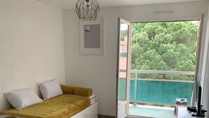 Een kleine slaapkamer met een bed, een tafeltje en een stoel. Er is een raam met uitzicht op groen.