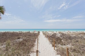 A sandy beach path leading to the ocean, surrounded by dunes and a wooden fence.