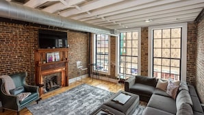 Una sala de estar con pared de ladrillo, chimenea, sofá y ventanas grandes.