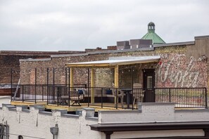 Une terrasse sur le toit avec un espace salon couvert, un mur de briques orné de graffitis et, au fond, un bâtiment surmonté d’un toit végétalisé.
