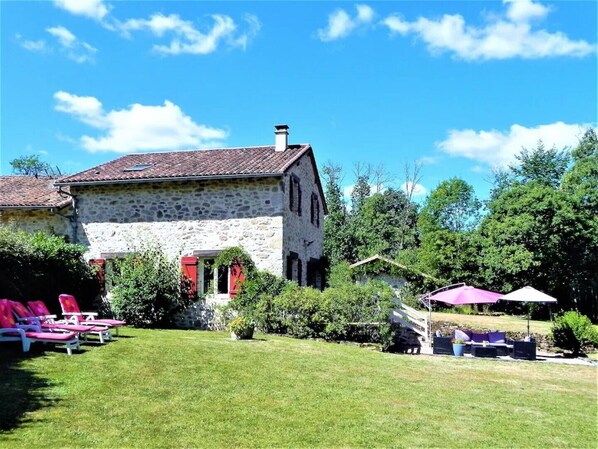 A stone building with a red-tiled roof, a grassy yard, and outdoor seating with umbrellas.