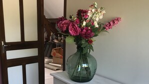 A room with a white dresser, a green vase with flowers, and boxes labeled "SEYNAVE" on the floor.