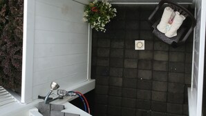 Um espaço ao ar livre pequeno e fechado, com uma parede revestida de azulejos pretos, um banco branco e uma lixeira preta.