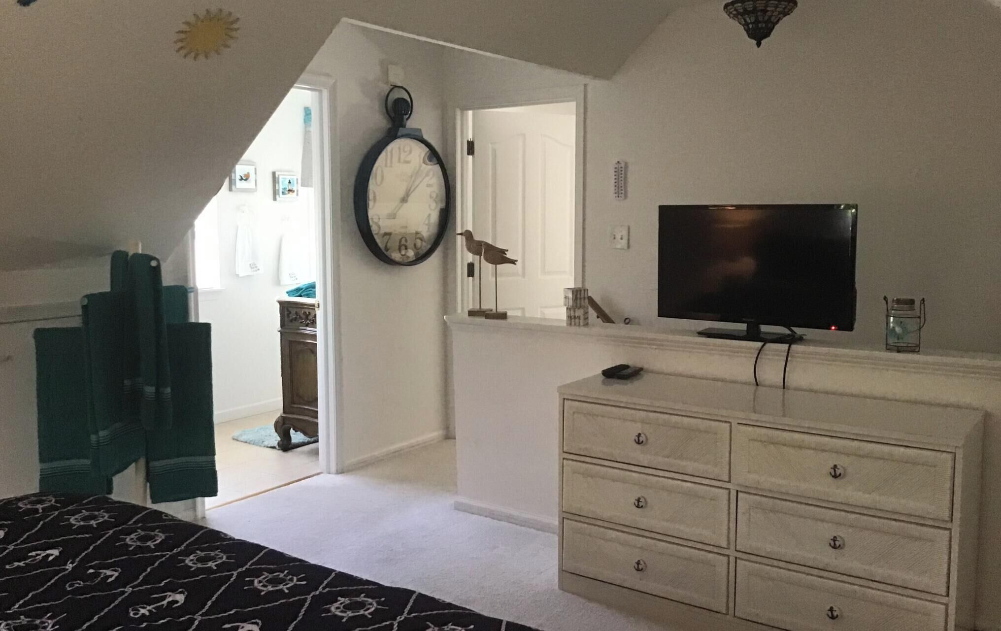 A bedroom with a bed, dresser, TV, and a clock on the wall.