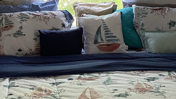 Quarto com cama, cortinas brancas, decorações de estrelas-do-mar e janela com vista para árvores.