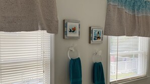 Casa de banho com duas janelas, cada uma com um porta-toalhas e um quadro emoldurado.