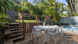 Une terrasse extérieure avec une plateforme en bois, des chaises en métal blanc, une table et un barbecue.