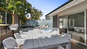 Un espace aménagé au bord de la piscine, avec une table et des chaises blanches, un barbecue et une vue sur la piscine.