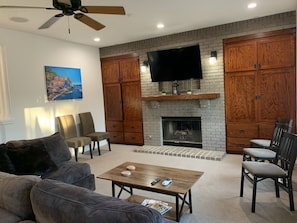 A living room with a fireplace, a ceiling fan, and a flat-screen TV mounted above it.