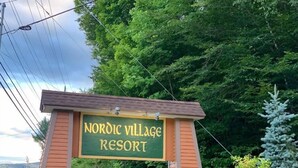 A sign for Nordic Village Resort with a stone and wood structure, surrounded by lush greenery and flowering plants. - Clean, quiet and cozy mountain get away Condo (Bartlett,)