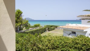 Vista costera amb cel serè, una muntanya lluny i un edifici blanc amb teulada de rajola.