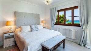 Un dormitori amb un llit gran, dues taules de nit amb làmpades, una panxa, una finestra amb cortines i un penjador de cristall.