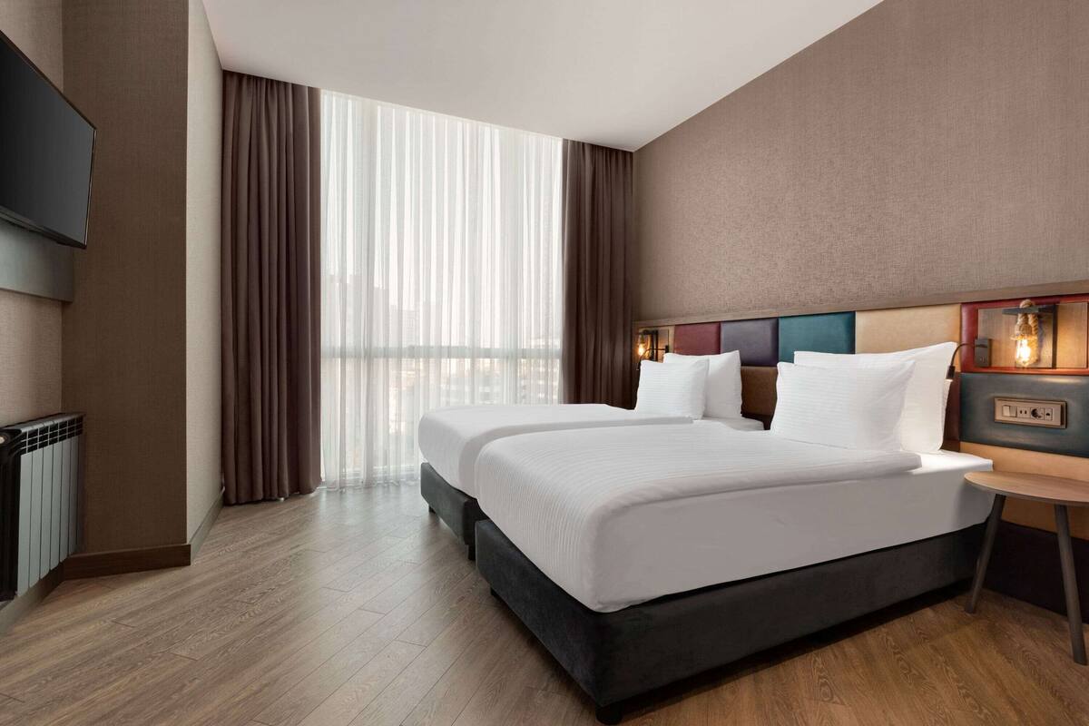 A hotel room with a large bed, a TV, and a view of the city.
