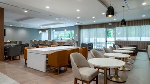 A modern hotel lobby with a central bar area, seating arrangements, and large windows providing natural light.