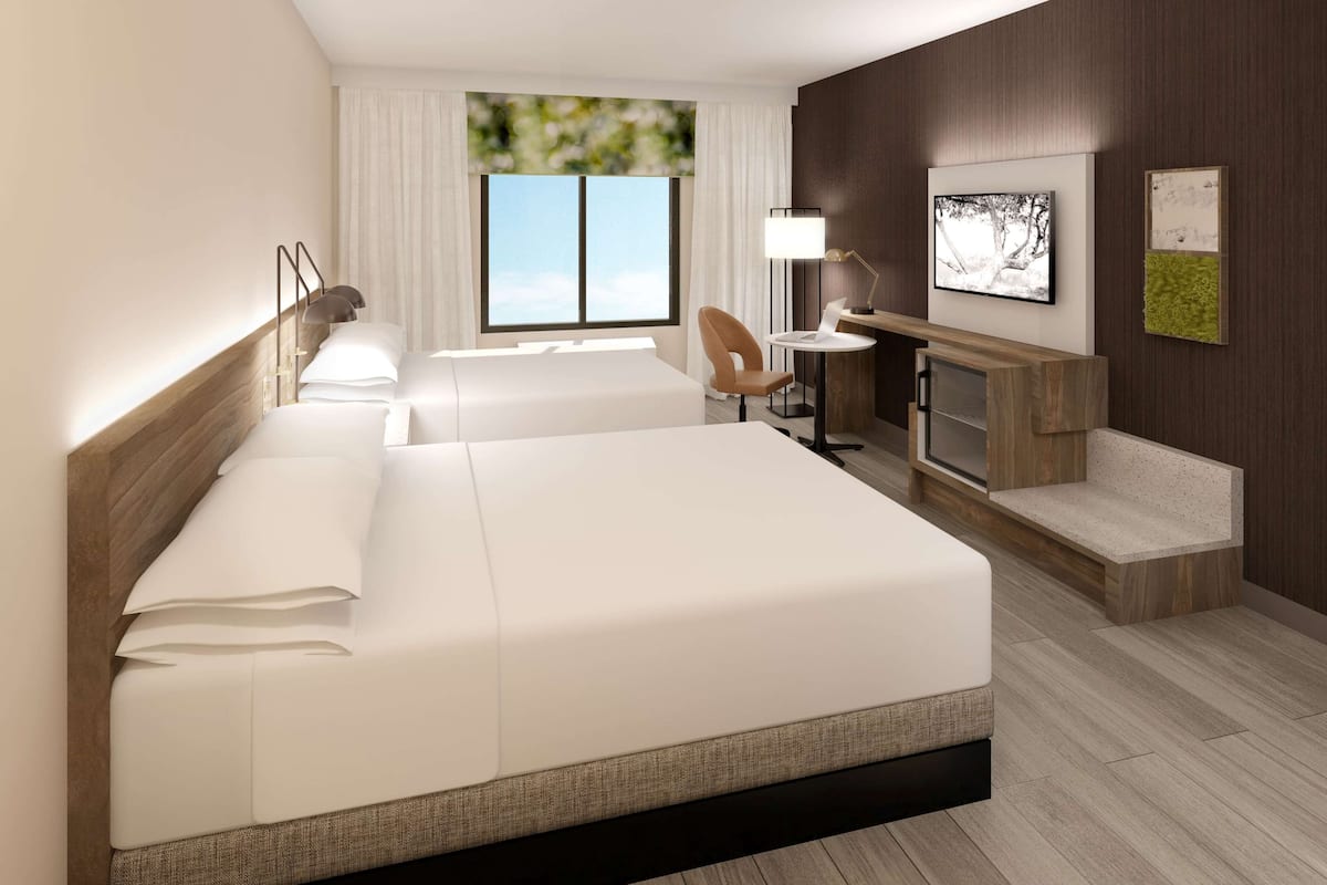 Habitación de hotel con una cama grande, un escritorio, una silla y un televisor en la pared.