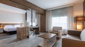 A modern hotel room with a bed, a desk, a chair, a sofa, and a large window.