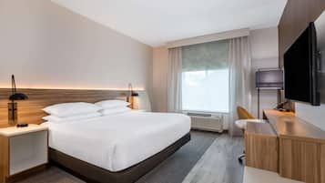 Une chambre d’hôtel moderne dotée d’un grand lit, de tables de chevet, d’un bureau, d’un téléviseur à écran plat et d’une fenêtre avec des rideaux.