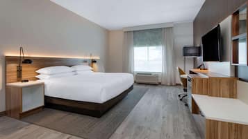 Quarto de hotel moderno com uma cama grande, uma escrivaninha, televisão de tela plana e uma janela com cortinas.