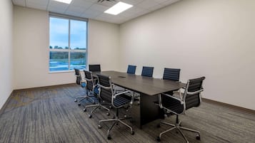 A conference room with a large table, six chairs, and a large window with a view of a sports field.