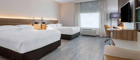 Quarto de hotel com duas camas, uma escrivaninha, uma cadeira, uma televisão e uma janela grande.