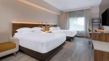 A hotel room with two beds, a sofa, a desk, and a TV.