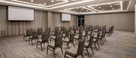 A conference room with rows of chairs, a large screen, and a carpeted floor.