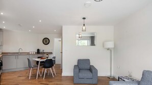 Ein modernes Wohnzimmer mit grauem Sofa, einem Essbereich mit Tisch und Stühlen, einer Küche mit grauen Schränken und einem großen Spiegel an der Wand.