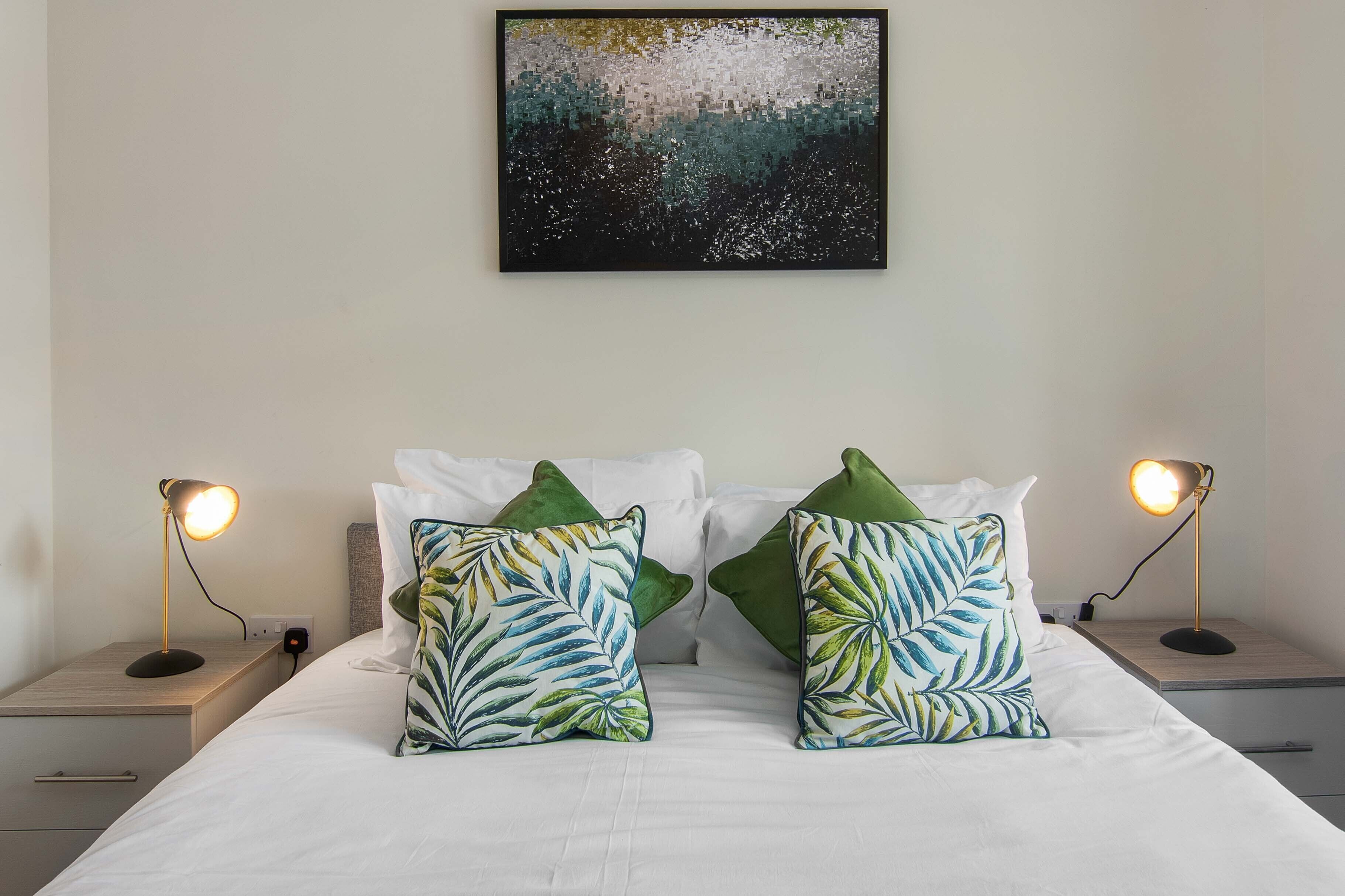 A neatly made bed with white linens, two green decorative pillows, and two bedside lamps on wooden nightstands.