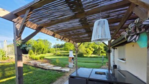 An outdoor patio with a grill, wicker furniture, and a pergola with a hanging light fixture.