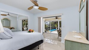 A bedroom with a bed, a ceiling fan, a large mirror, and a view of the outdoors through a sliding glass door. - Family-friendly villa w/bikes & pool table; Gulf access! Villa Lilly - SWFL Rentals (Cape Coral)