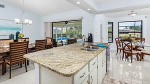 A modern kitchen with a granite countertop, stainless steel sink, and a dining area with wooden chairs and a glass table. - Family-friendly villa w/bikes & pool table; Gulf access! Villa Lilly - SWFL Rentals (Cape Coral)