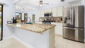 A modern kitchen with granite countertops, stainless steel appliances, and white cabinetry. - Family-friendly villa w/bikes & pool table; Gulf access! Villa Lilly - SWFL Rentals (Cape Coral)