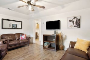 Ein Wohnzimmer mit Ledersofa, Fernseher, Deckenventilator und einem gerahmten Bild an der Wand.