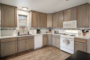 A kitchen with wooden cabinets, a white microwave, a stove, and a sink. - Cherry Street | Near Main | Gas BBQ | Couples (Bandera)