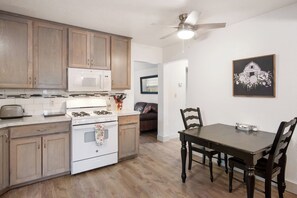 A kitchen with wooden cabinets, a white stove, and a dining table with chairs. - Cherry Street | Near Main | Gas BBQ | Couples (Bandera)