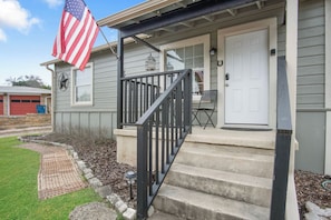 Ein Wohnhaus mit Veranda, einer weißen Tür, einer kleinen Sitzgelegenheit im Freien und einer amerikanischen Flagge.