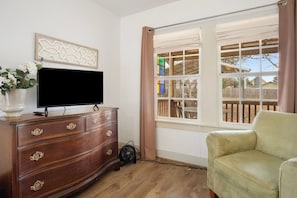 Ein Zimmer mit einem hölzernen Schminktisch, einem Fernseher, einem Fenster mit Vorhängen und einem grünen Sessel.