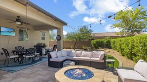 An outdoor patio with a round fire pit, a covered seating area with a sofa and chairs, a dining table, and a TV mounted on the wall. - Desert Oasis with pool and spa in gated community (Laveen)