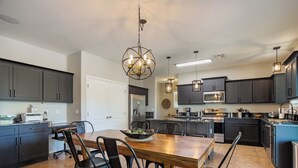 A modern kitchen with dark cabinets, a wooden dining table, and black chairs. - Desert Oasis with pool and spa in gated community (Laveen)