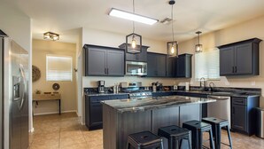 A modern kitchen with dark cabinets, a large island with stools, a stainless steel refrigerator, and a microwave. - Desert Oasis with pool and spa in gated community (Laveen)