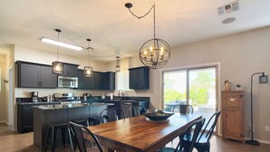 A modern kitchen with dark cabinets, a central island, and a dining area with a wooden table and chairs. - Desert Oasis with pool and spa in gated community (Laveen)